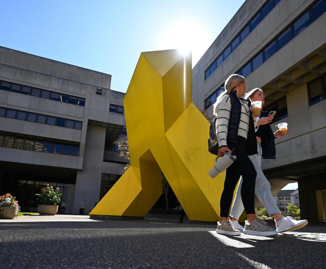 Two students walk and talk beside a yellow sculpture